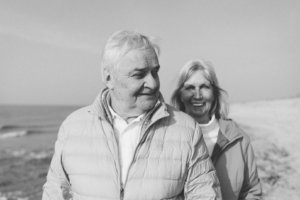 Paarshooting am Strand – Glückliches Paarfoto zum 50. Ehejubiläum Lachendes Ehepaar im Schwarz-Weiß-Porträt beim Paarshooting am Strand von Rostock – sie stehen eng beieinander mit Blick auf die Ostsee, anlässlich ihrer goldenen Hochzeit.